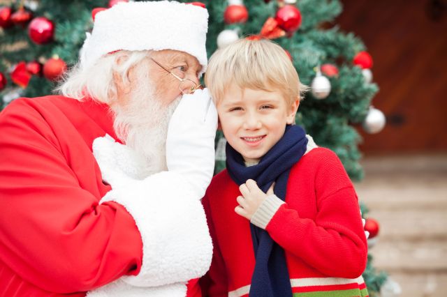 23726302 - santa claus whispering in boy's ear against christmas tree